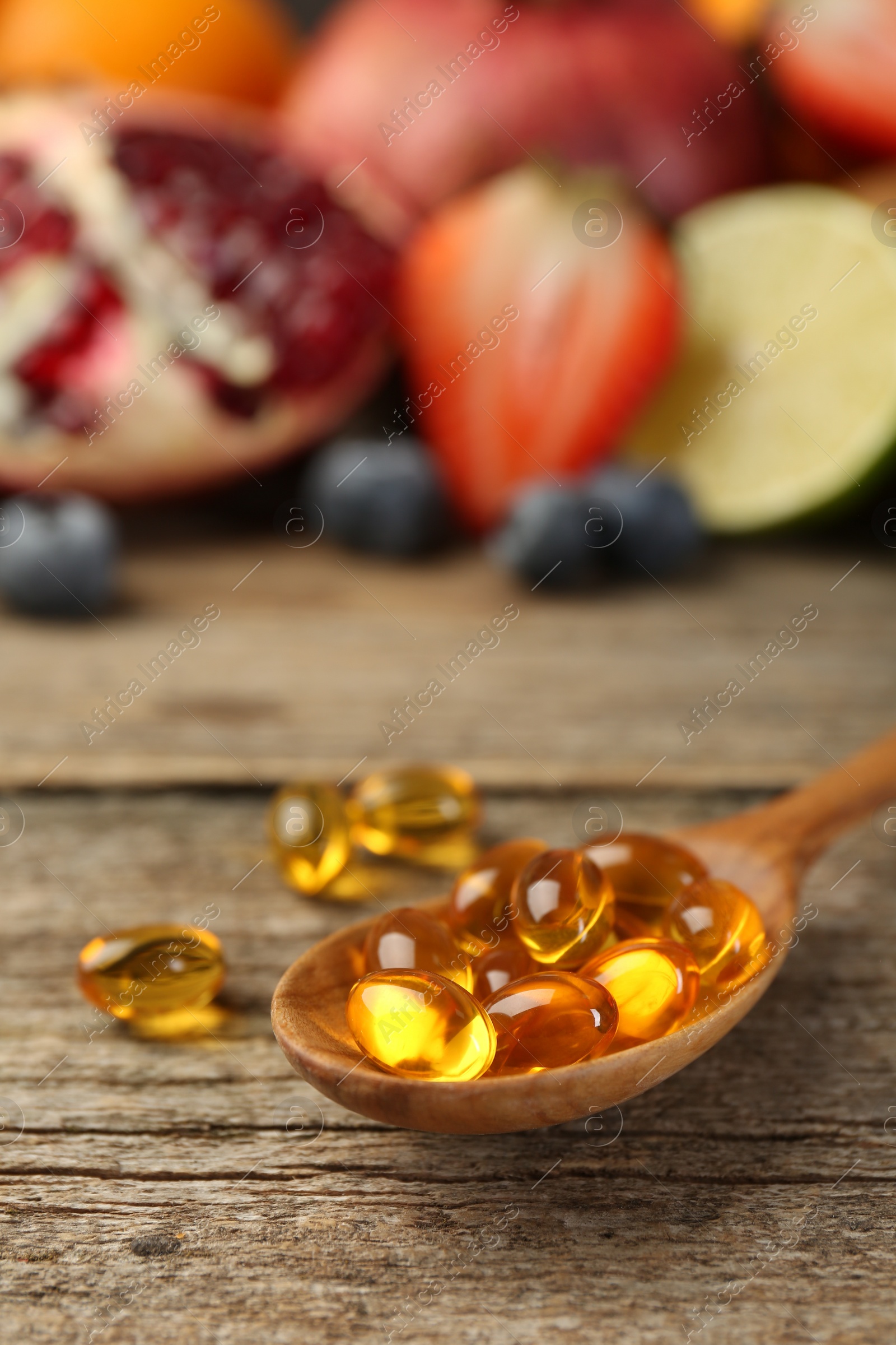 Photo of Vitamin pills in spoon and fresh fruits on wooden table