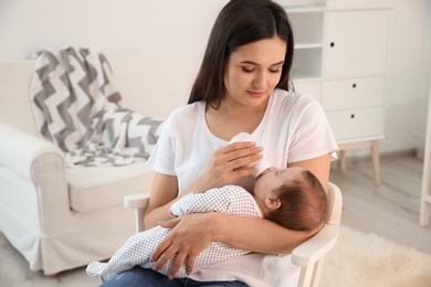 Photo of Woman feeding her baby from bottle in nursery at home