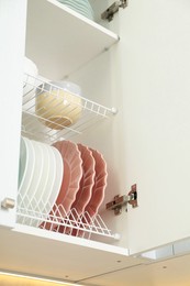Clean plates and bowls on shelves in cabinet indoors, low angle view