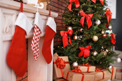 Photo of Beautiful Christmas tree and gifts near decorative fireplace with stockings indoors