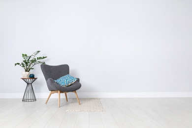 Photo of Stylish room interior with comfortable armchair and plant near white wall. Space for text