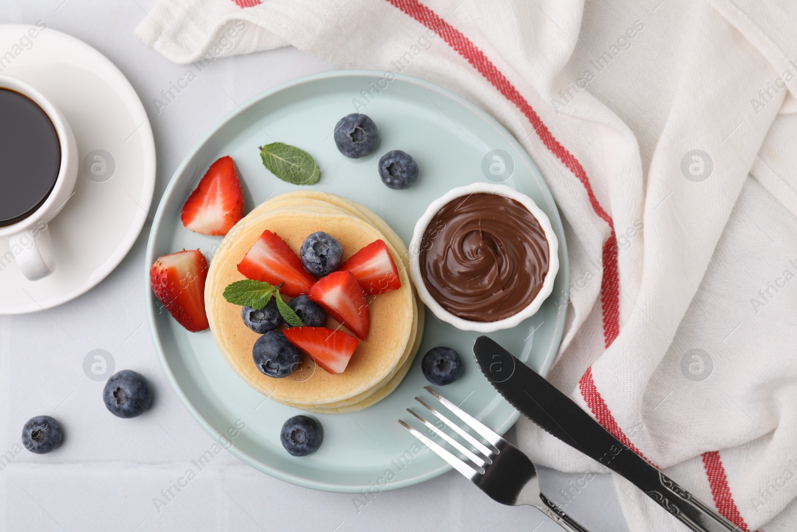 Photo of Delicious pancakes with strawberries, blueberries and chocolate sauce served on white tiled table, flat lay