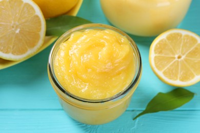 Photo of Delicious lemon curd in glass jar, fresh citrus fruit and green leaves on light blue wooden table, closeup