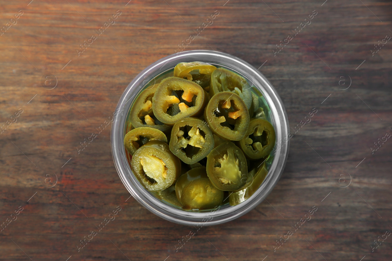 Photo of Glass jar of pickled green jalapeno peppers on wooden table, top view