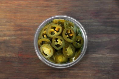 Photo of Glass jar of pickled green jalapeno peppers on wooden table, top view