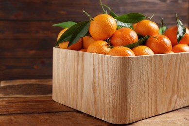 Photo of Fresh tangerines with green leaves in crate on wooden table, closeup