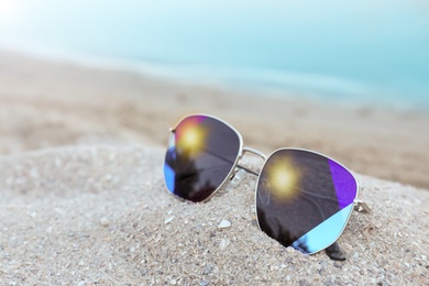 Photo of Stylish sunglasses on sandy beach near sea. Space for text