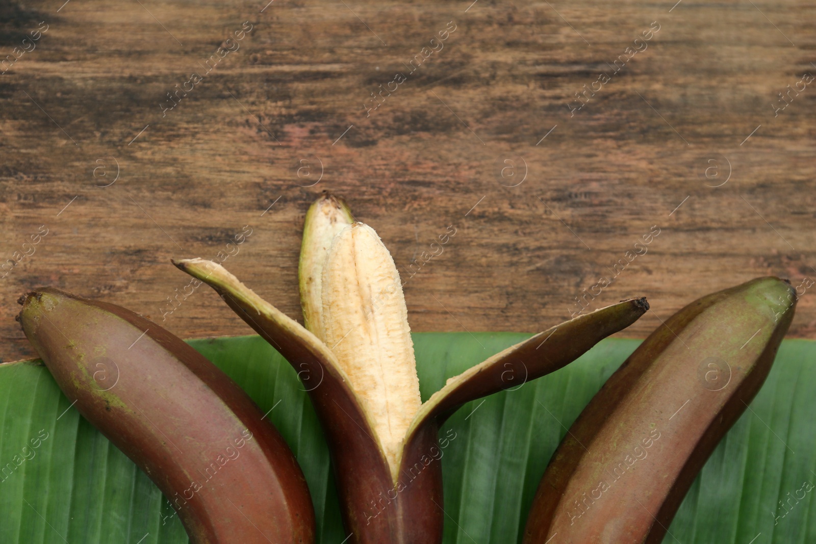 Photo of Delicious purple bananas and fresh leaf on wooden table, closeup. Space for text