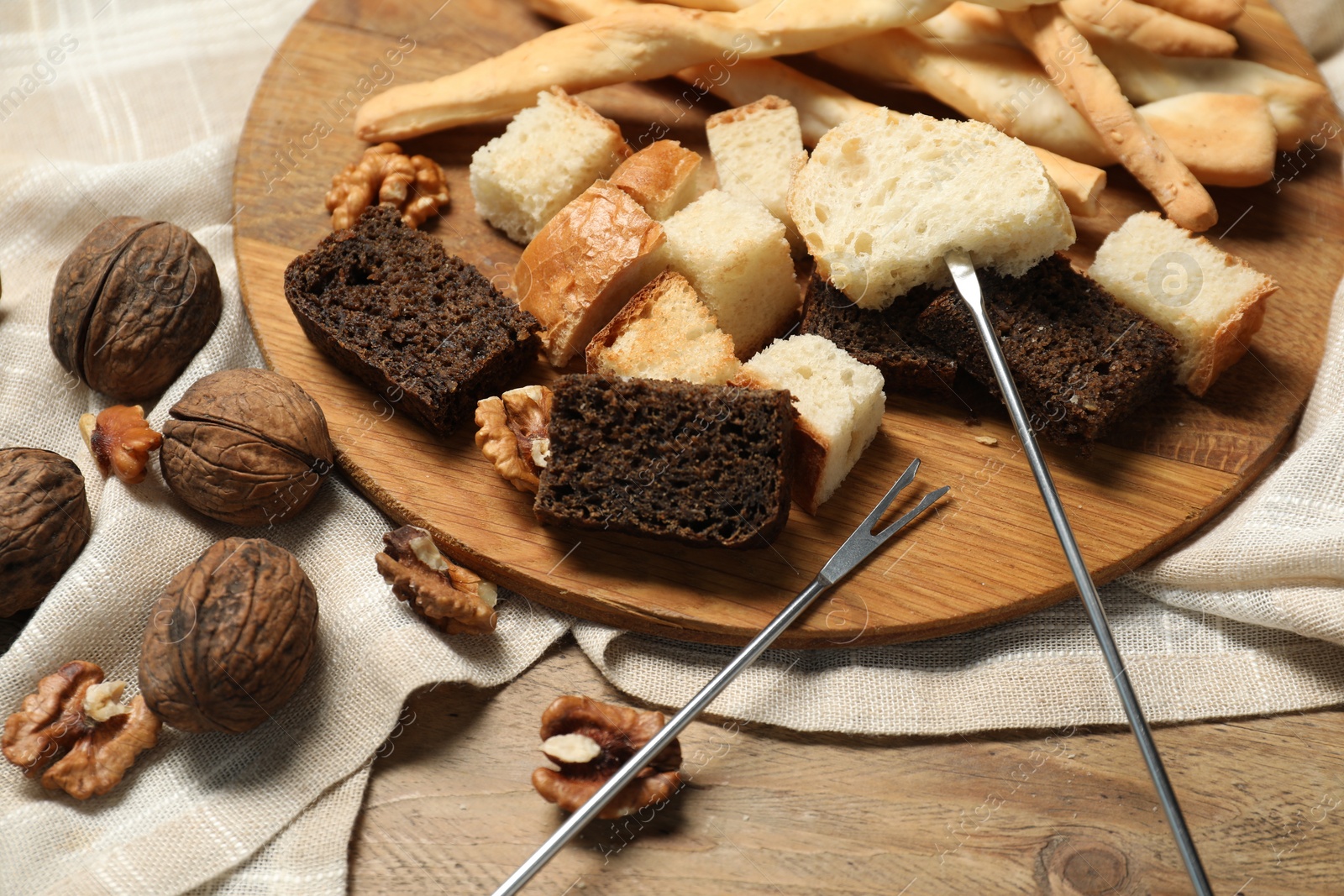 Photo of Fondue forks with pieces of bread and nuts on wooden table, closeup