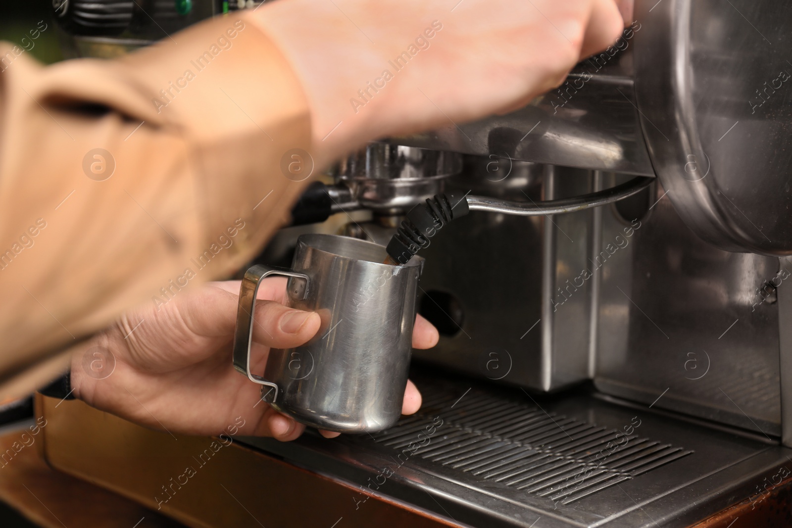 Photo of Barista steaming milk using coffee machine, closeup