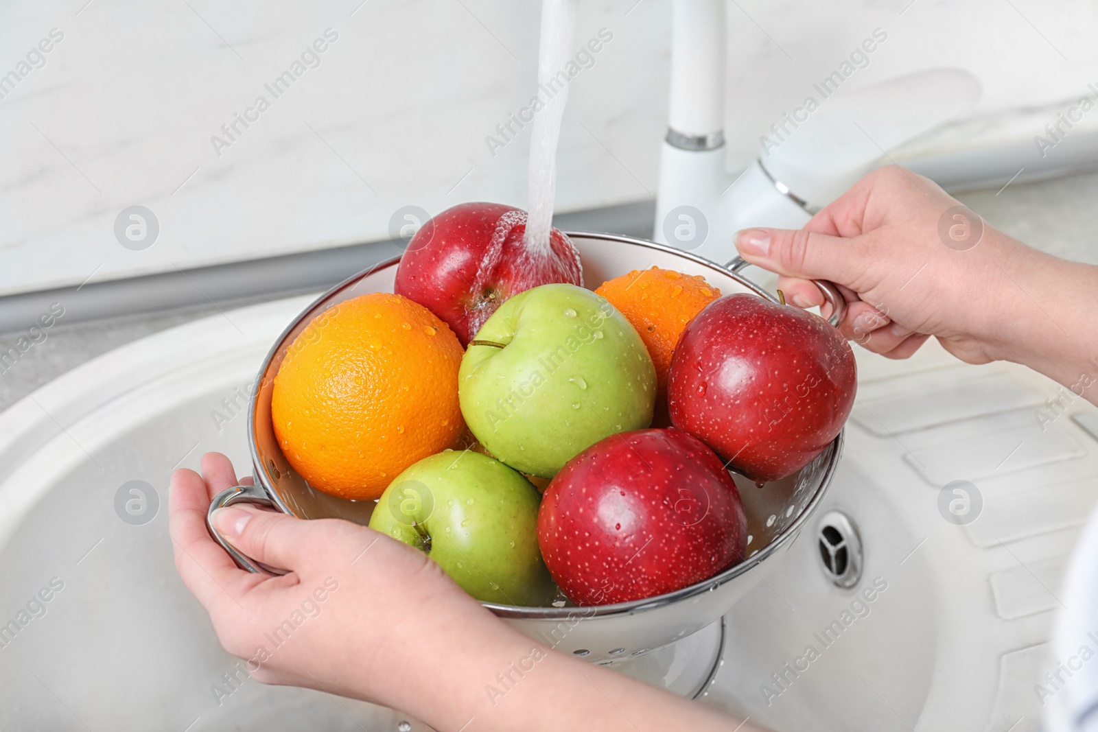 Photo of Woman washing fresh fruits in colander under water, closeup