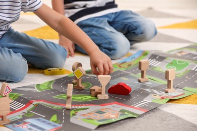Photo of Little children playing with set of wooden road signs and toy cars indoors, closeup