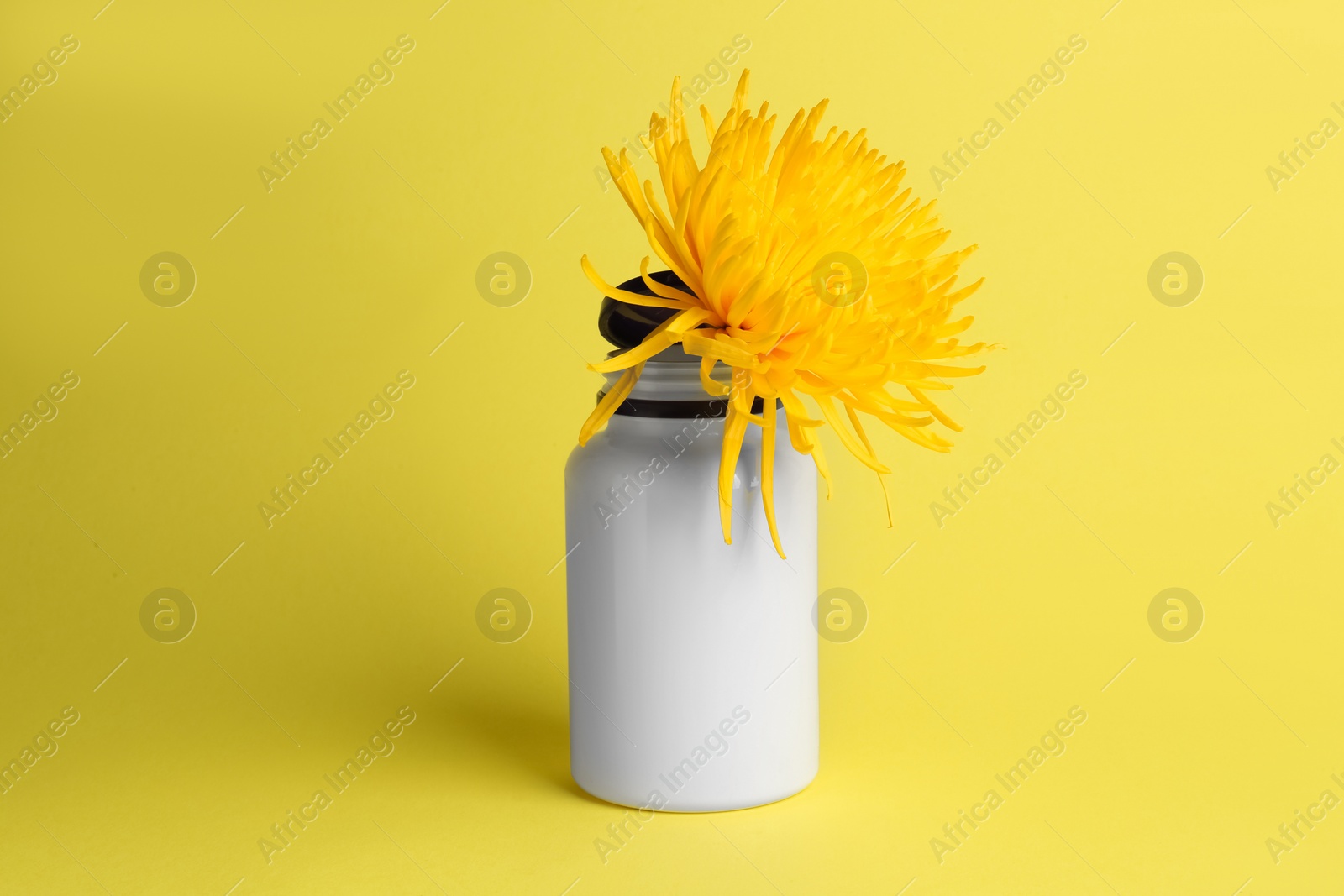 Photo of Medicine bottle and flower on yellow background