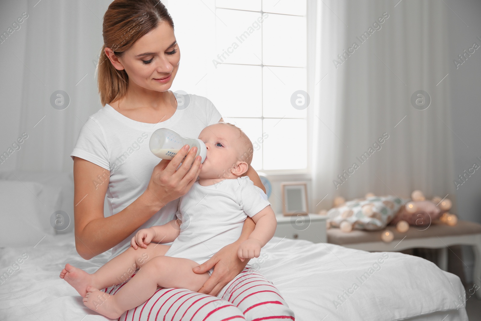 Photo of Lovely mother feeding her baby from bottle on bed at home. Space for text