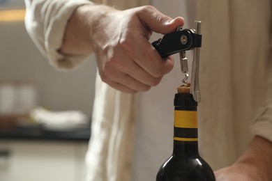 Man opening wine bottle with corkscrew on blurred background, closeup