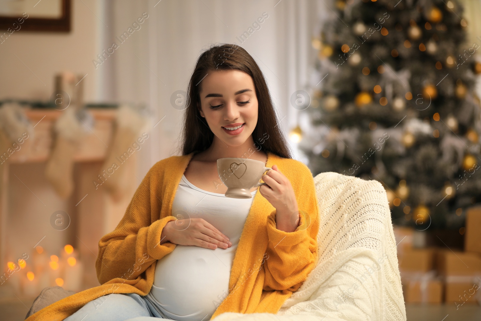 Photo of Happy pregnant woman in armchair at room decorated for Christmas. Expecting baby