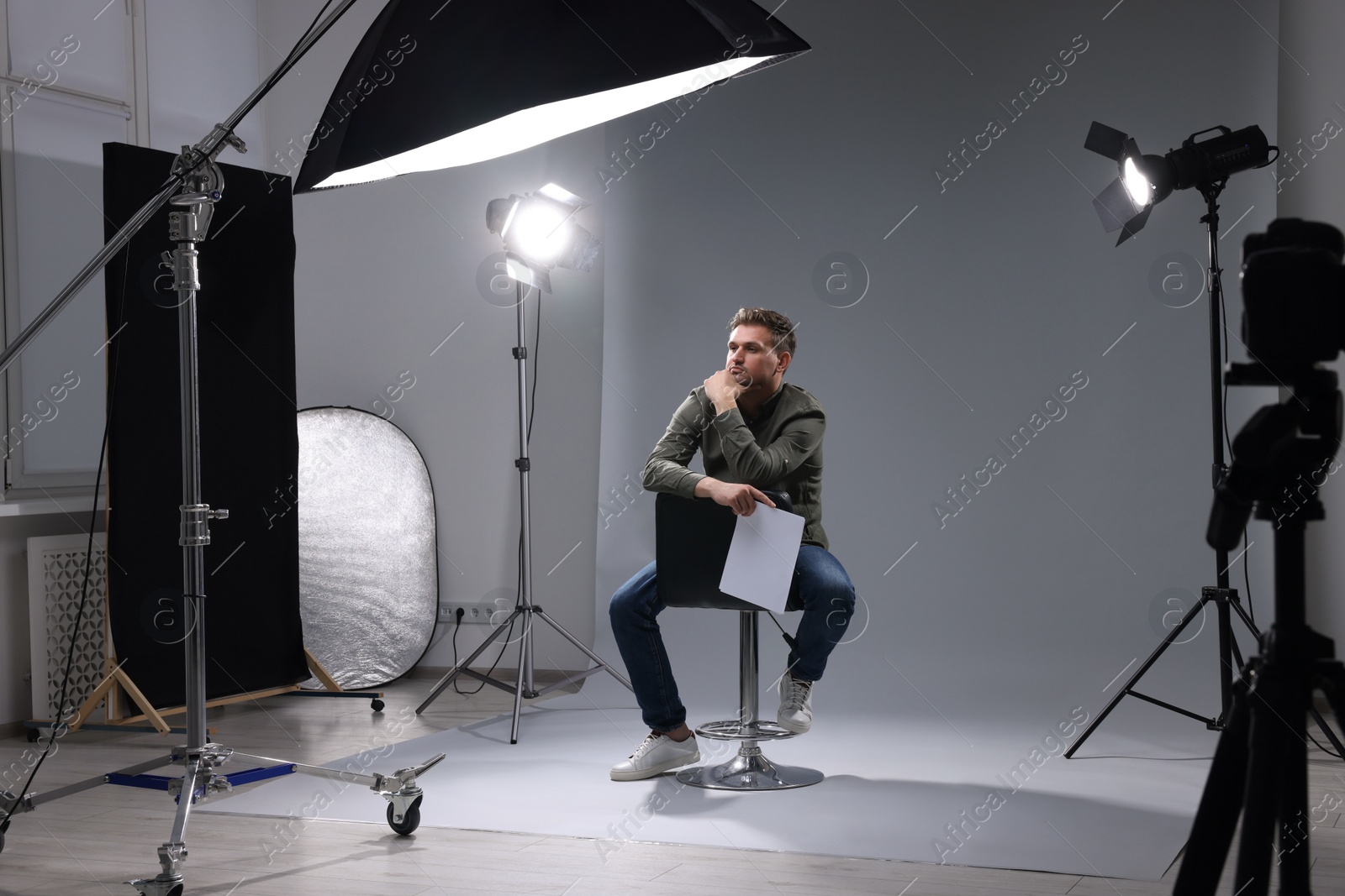 Photo of Casting call. Man with script sitting on chair against grey background in studio