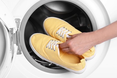 Woman putting pair of sport shoes into washing machine, closeup