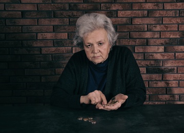 Poor mature woman counting coins at table