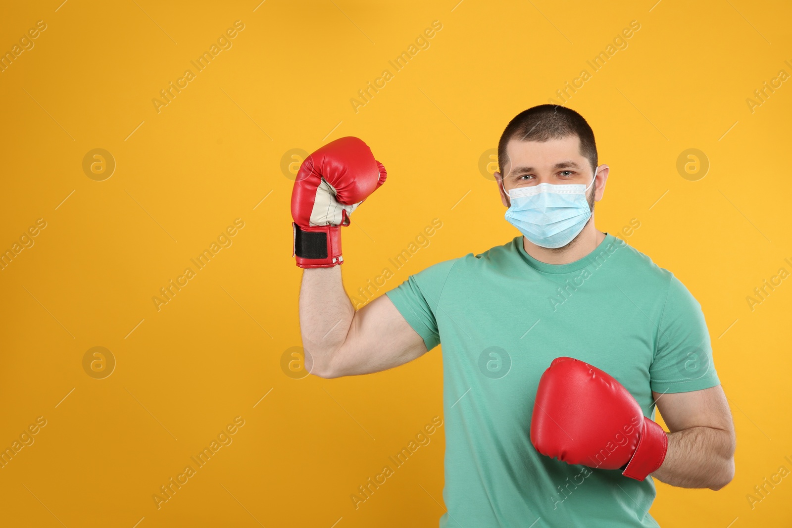 Photo of Man with protective mask and boxing gloves on yellow background, space for text. Strong immunity concept