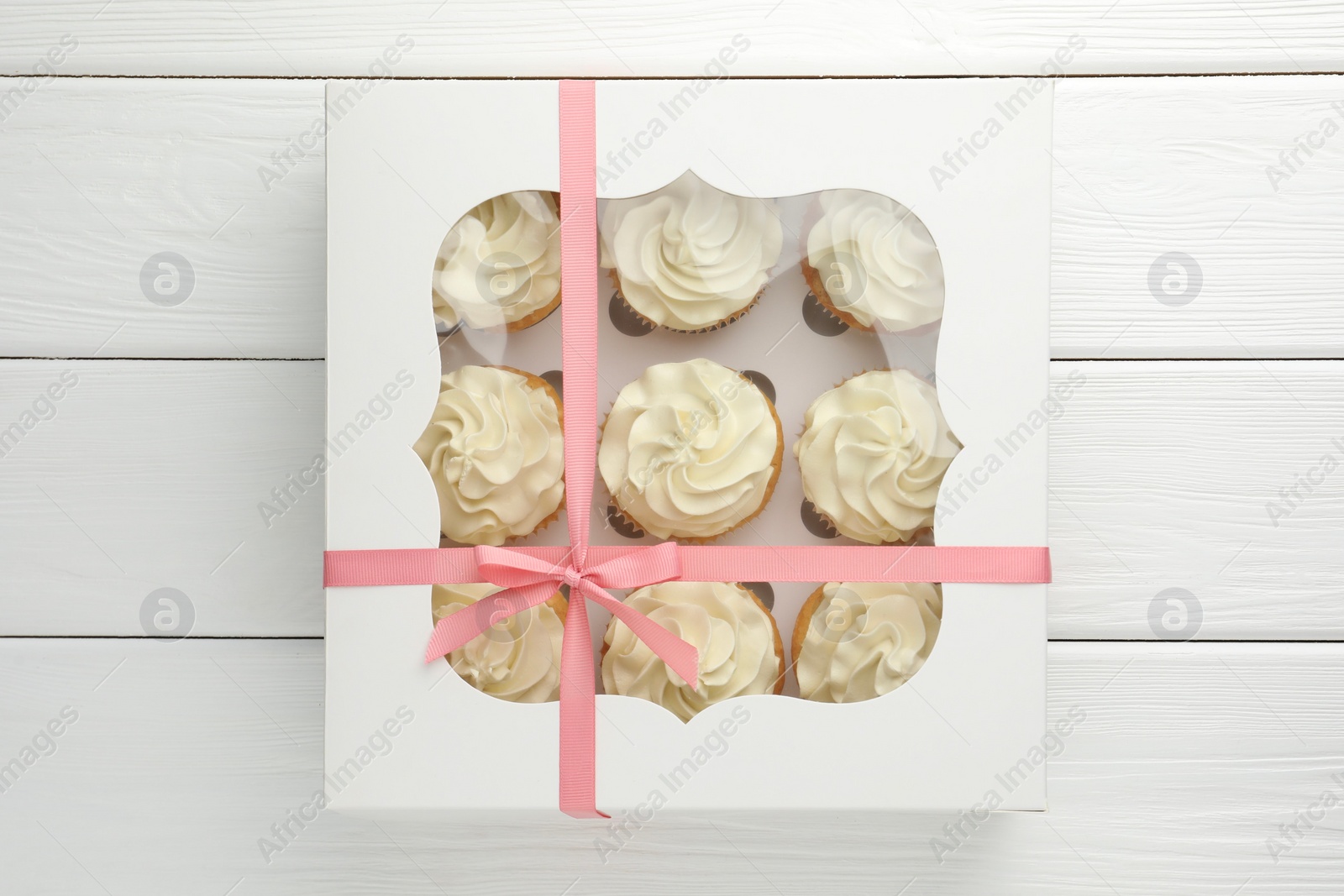 Photo of Tasty cupcakes with vanilla cream in box on white wooden table, top view