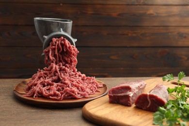 Photo of Manual meat grinder with beef and parsley on wooden table, space for text