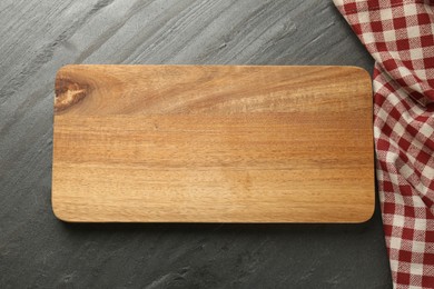 Photo of Wooden cutting board and kitchen towel on dark grey table, top view