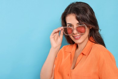 Photo of Happy beautiful woman with stylish sunglasses on light blue background, space for text