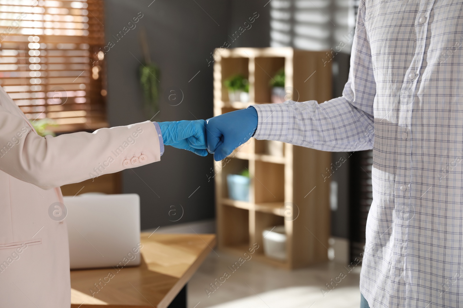 Photo of People greeting each other by bumping fists instead of handshake in office, closeup
