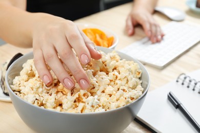 Photo of Bad habits. Woman eating popcorn while working on computer at table, closeup