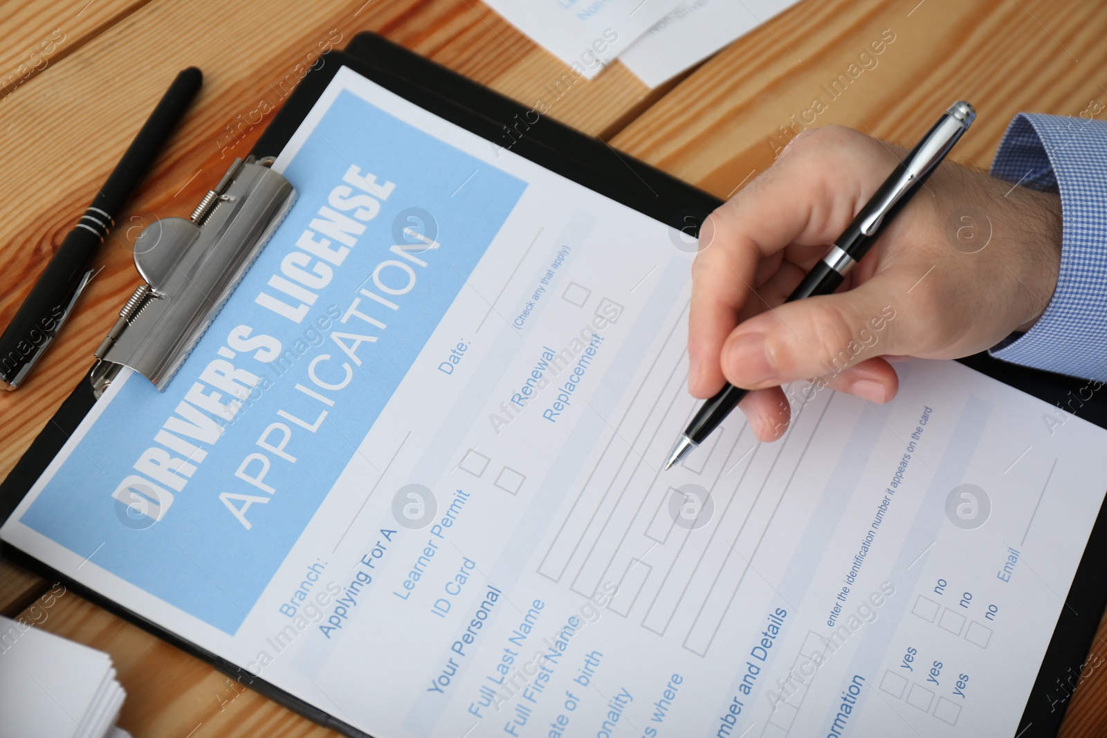 Photo of Man filling in driver's license application form at wooden table, closeup