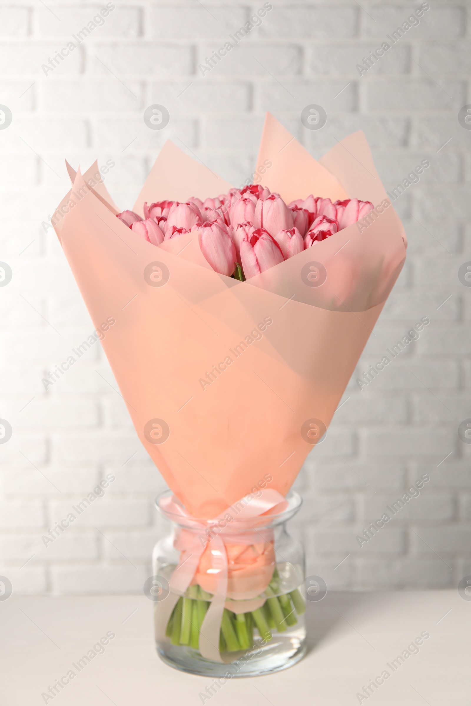 Photo of Bouquet of beautiful pink tulips in vase on white table near brick wall