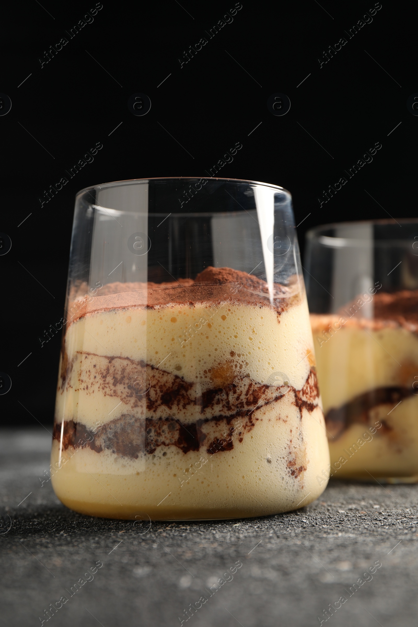 Photo of Delicious tiramisu in glasses on grey textured table, closeup