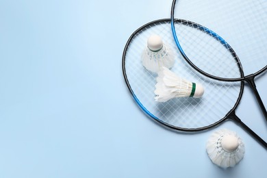 Photo of Feather badminton shuttlecocks and rackets on light blue background, flat lay. Space for text