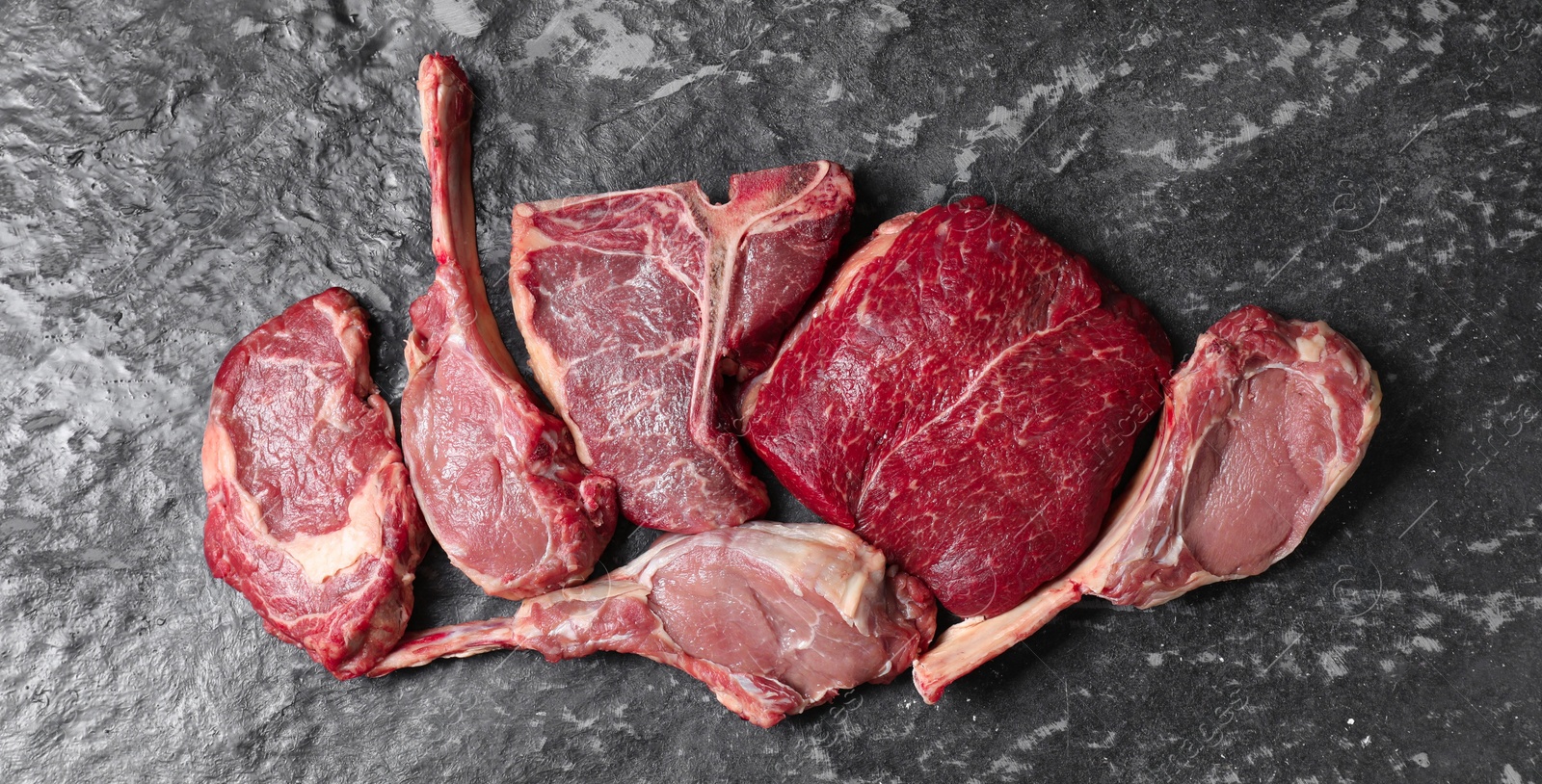 Photo of Fresh raw beef cuts on grey textured table, flat lay