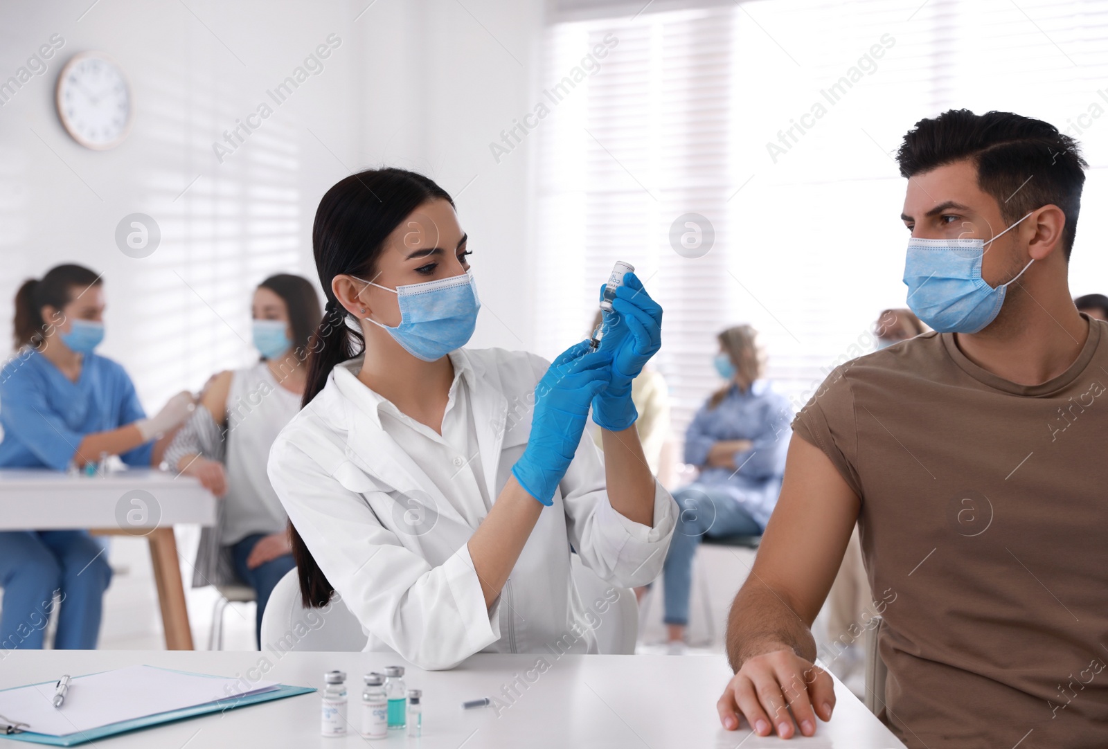 Photo of Doctor giving injection to patient while other waiting in line at hospital. Vaccination campaign