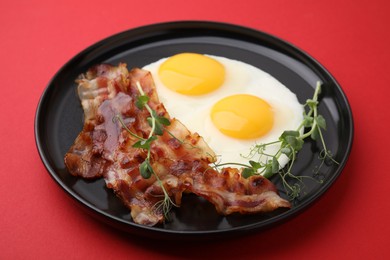 Fried eggs, bacon and microgreens on red background