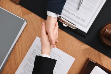 Notary shaking hands with client at wooden table, top view