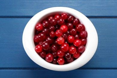 Photo of Fresh cranberries in bowl on blue wooden table, top view