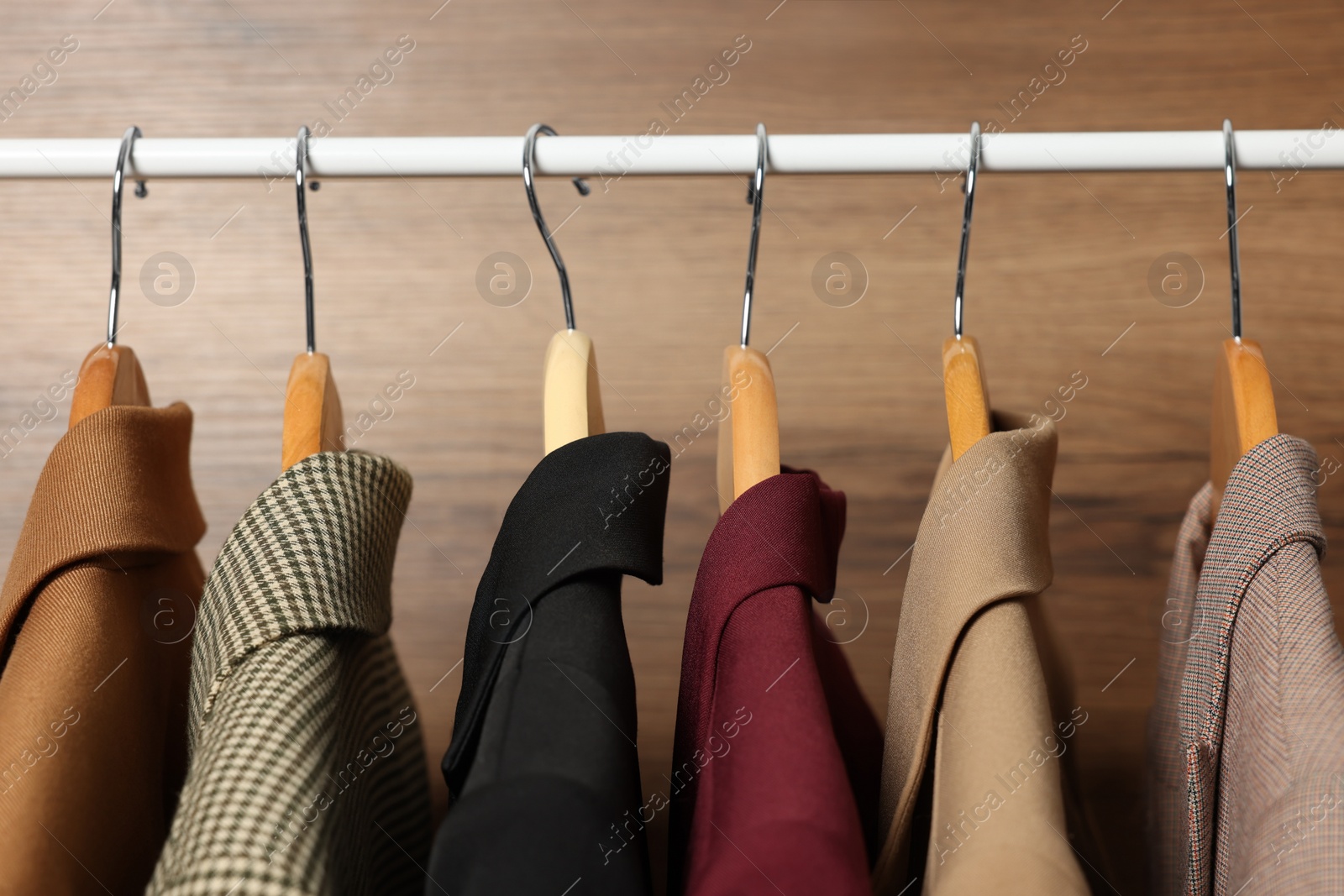 Photo of Hangers with stylish women`s clothes on rack near wooden wall, closeup