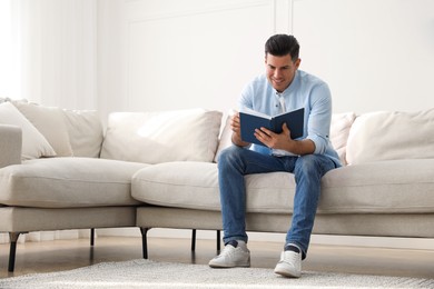 Man with book sitting on comfortable sofa in living room