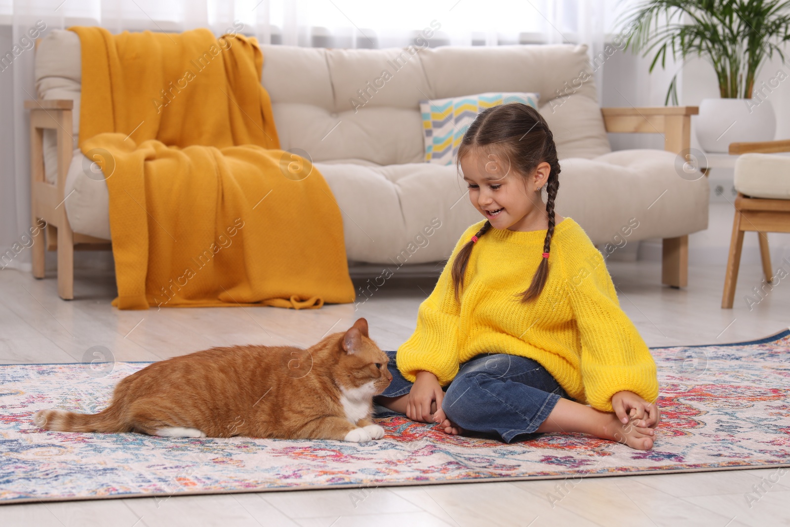 Photo of Happy little girl and cute ginger cat on carpet at home