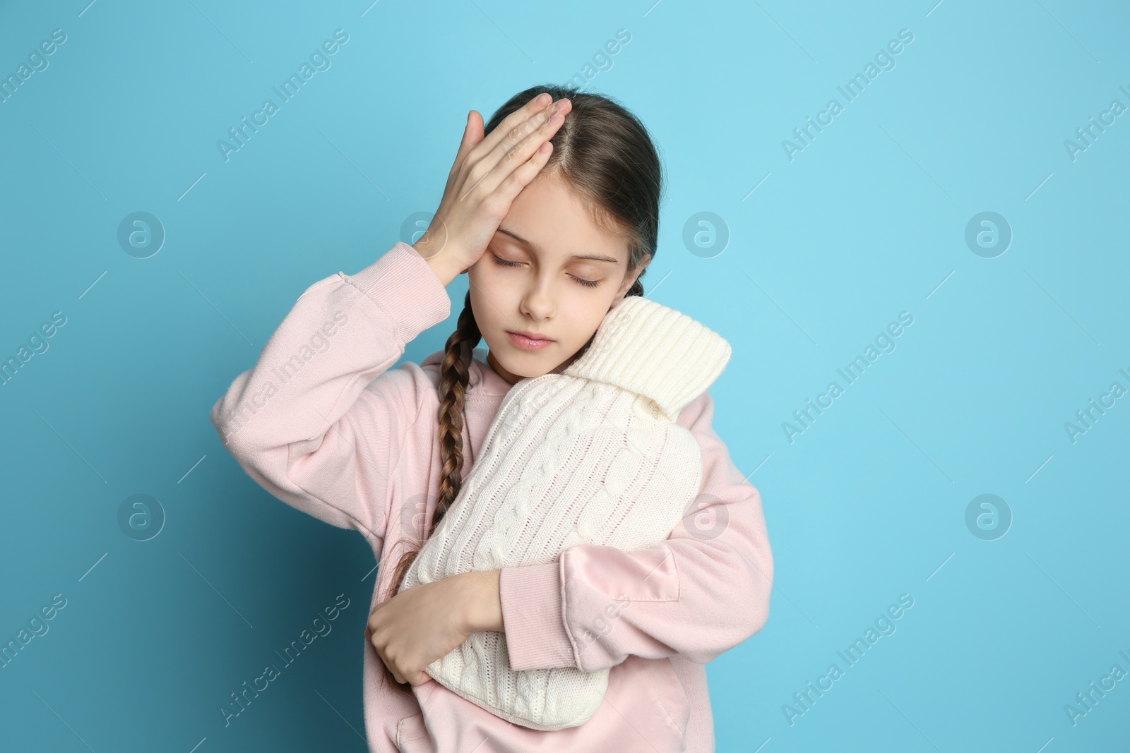 Photo of Ill girl with hot water bottle suffering from cold on light blue background