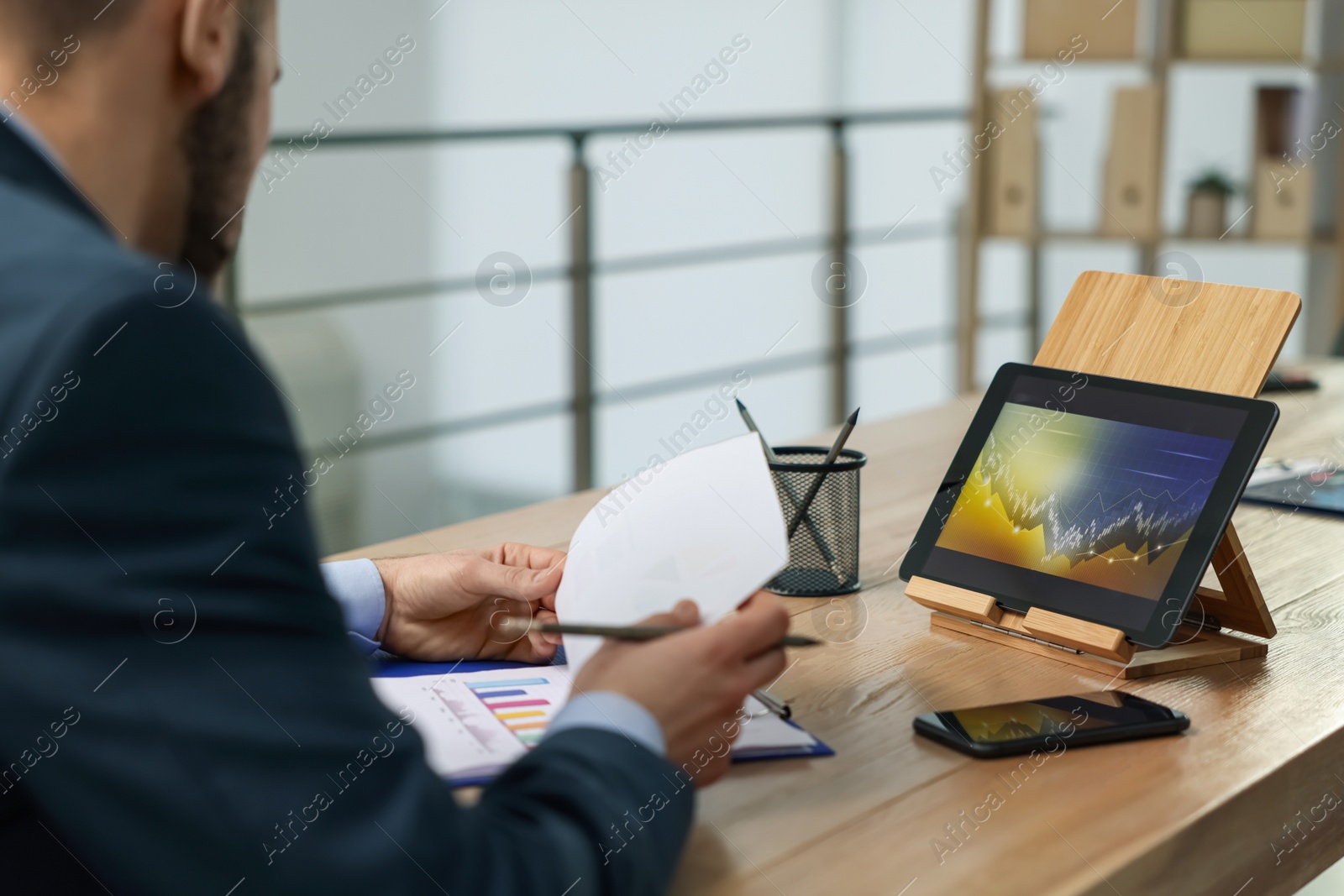 Photo of Broker working with tablet and documents at table in office. Forex trading