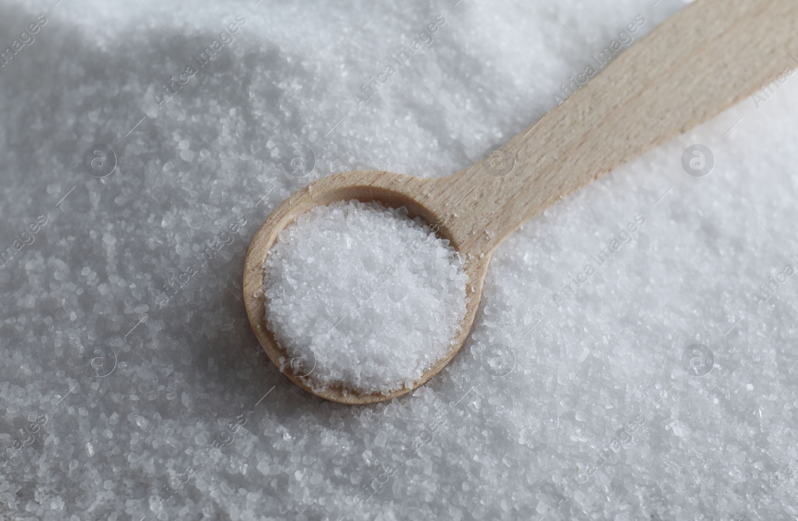 Photo of Wooden spoon on white sea salt, closeup