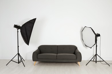 Photo of Comfortable sofa and professional lighting equipment in photo studio