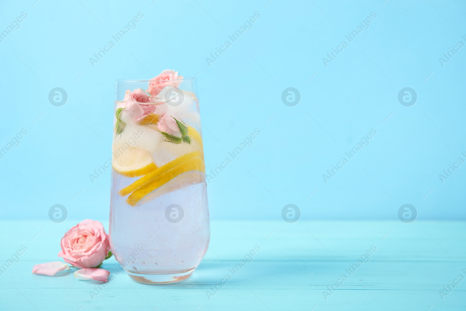 Photo of Tasty refreshing lemon drink with roses on wooden table against light blue background. Space for text