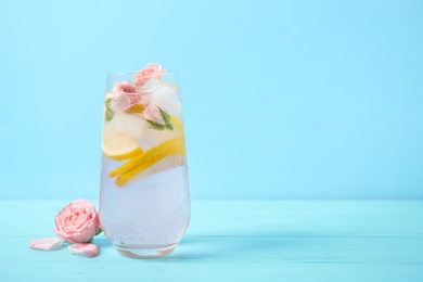 Photo of Tasty refreshing lemon drink with roses on wooden table against light blue background. Space for text