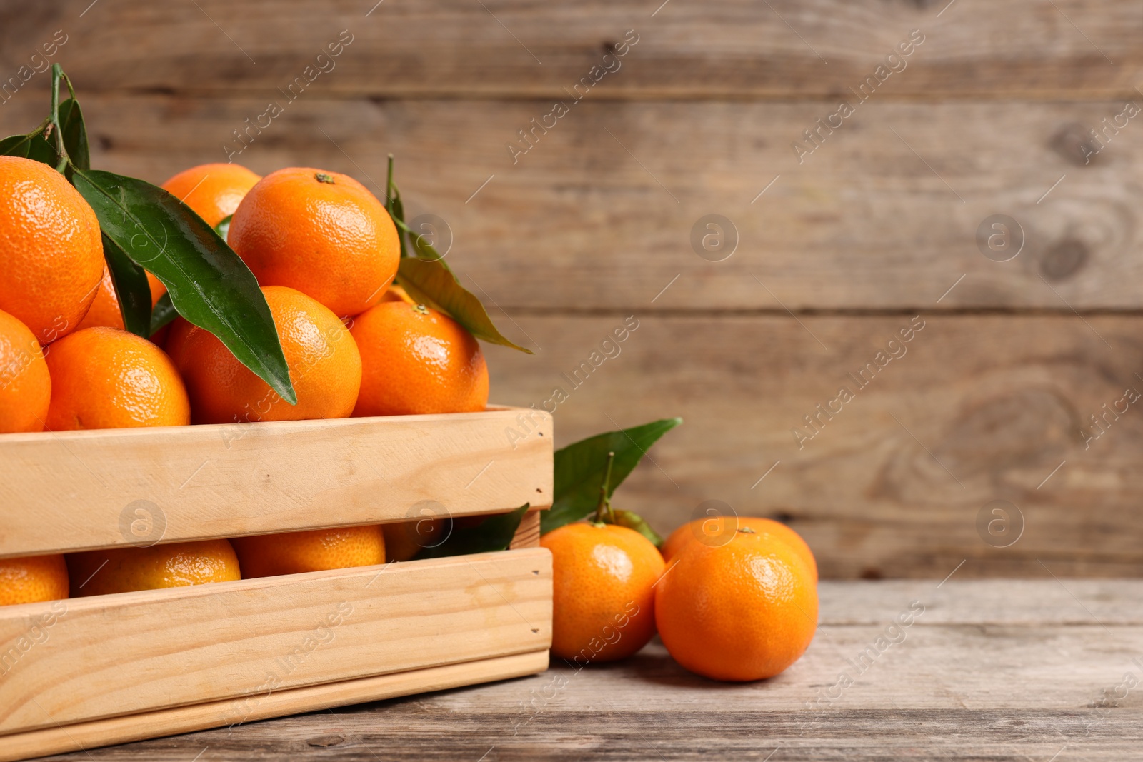 Photo of Delicious tangerines with leaves on wooden table, closeup. Space for text