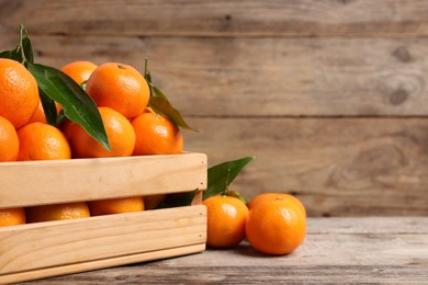 Delicious tangerines with leaves on wooden table, closeup. Space for text